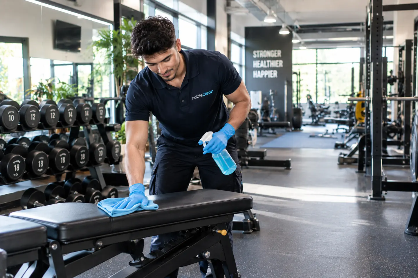 Mitarbeiter von nobleclean desinfiziert eine Hantelbank im Fitnessstudio.